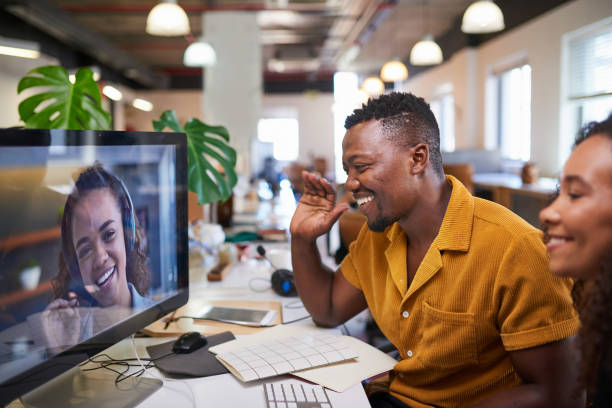 A remote employee of a project management company waves hello to his colleague on a video call.